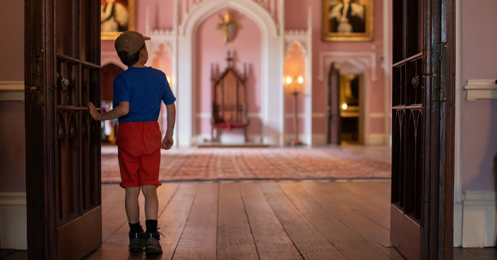 Little boy pearing into a room with a throne at Auckland Palace.